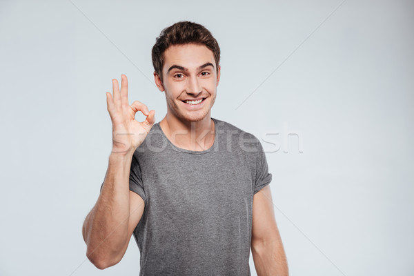Portrait of a cheerful young man showing okay gesture Stock photo © deandrobot