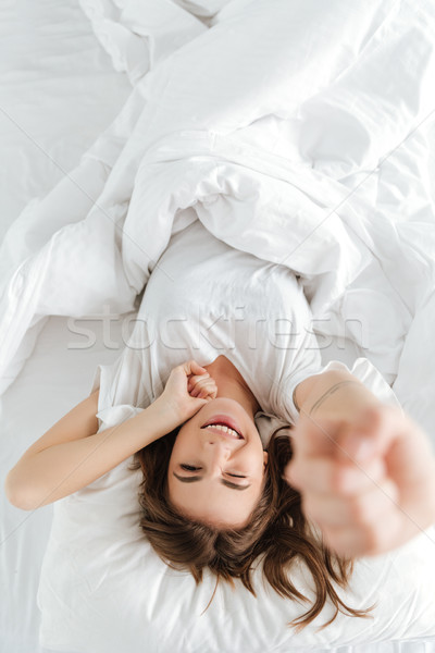 Pretty woman lies on bed at home indoors while stretching. Stock photo © deandrobot