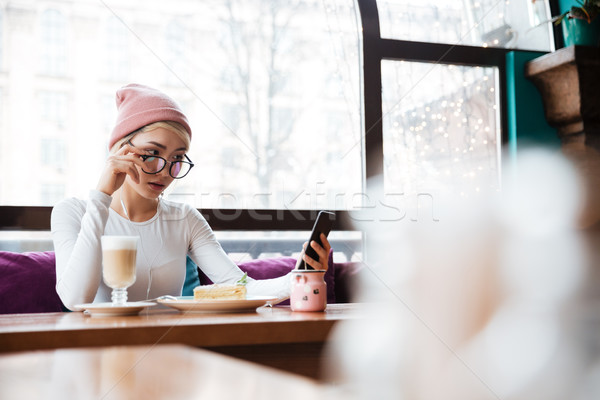 Serious young woman eating and using cell phone in cafe Stock photo © deandrobot
