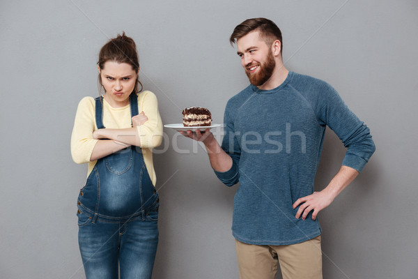 Smiling husband offers his unsatisfied pregnant wife a chocolate cake Stock photo © deandrobot