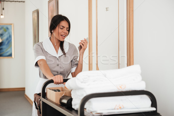 Young maid in earphones singing while walking with housekeeping cart Stock photo © deandrobot