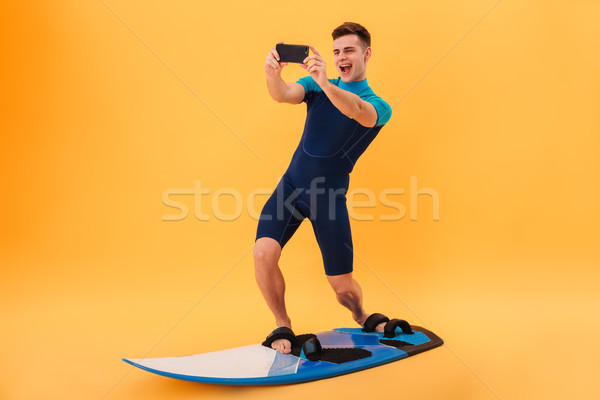Full length photo of young smiling man in swimsuit taking selfie Stock photo © deandrobot