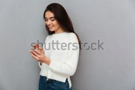 Happy pretty girl in white sweater using mobile phone Stock photo © deandrobot