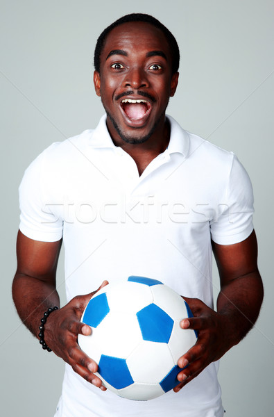 Funny african man holding soccer ball on gray background Stock photo © deandrobot