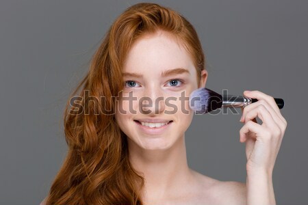 Smiling lovely young female applying powder blush brush for makeup Stock photo © deandrobot