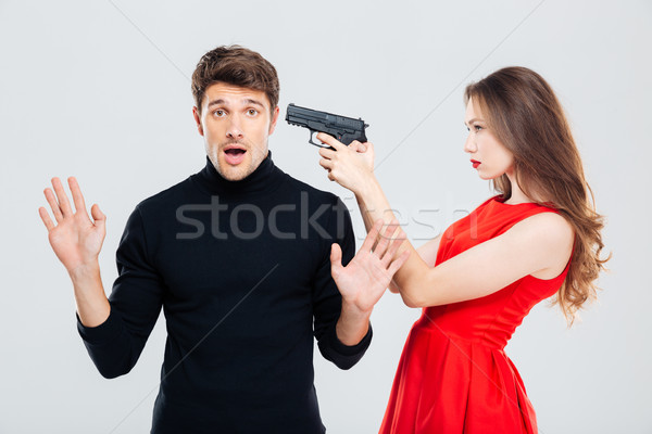 Woman standing and threatening with gun to scared young man Stock photo © deandrobot