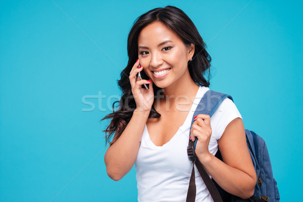 Smiling young asian woman with backpack talking on cellphone Stock photo © deandrobot