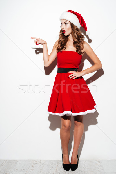 Shocked beautiful woman in red santa claus costume pointing away Stock photo © deandrobot