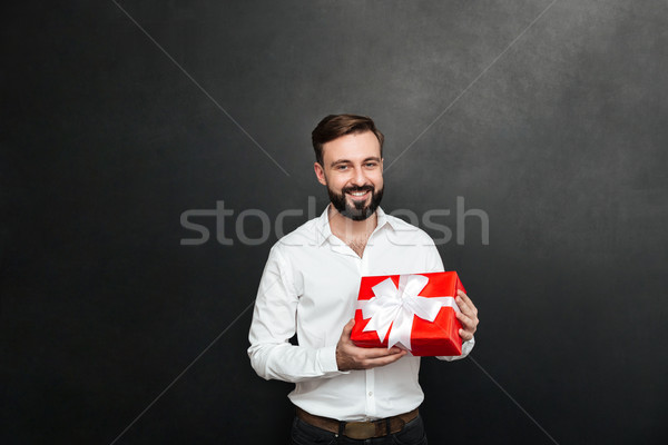 Portrait of happy bearded man holding red gift box and looking a Stock photo © deandrobot