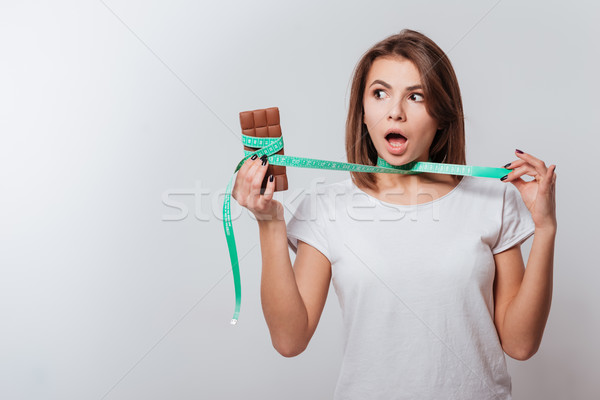 Young shocked lady holding centimeter and chocolate Stock photo © deandrobot