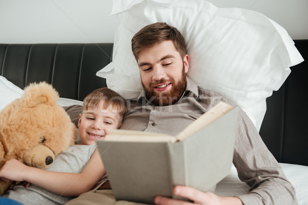 Boy lies near toy with his father reading fairytale book. Stock photo © deandrobot