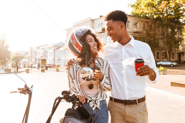 Happy young african couple drinking coffee while standing near motorbike Stock photo © deandrobot