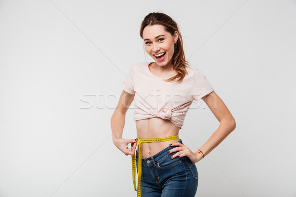 Portrait of a slim pleased woman holding measuring tape Stock photo © deandrobot