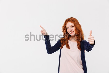 Cheerful pretty young redhead lady showing thumbs up while pointing. Stock photo © deandrobot