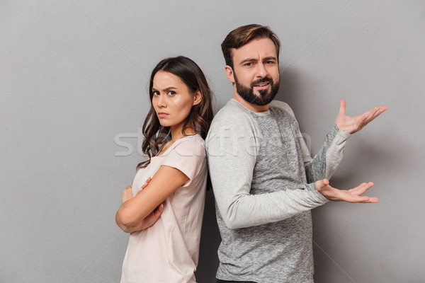 Stock photo: Portrait of a confused young couple standing back to back