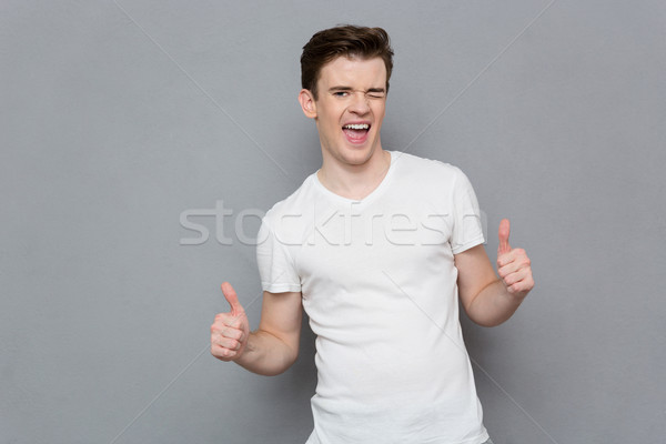 Happy young man giving thumbs up sign and winking Stock photo © deandrobot