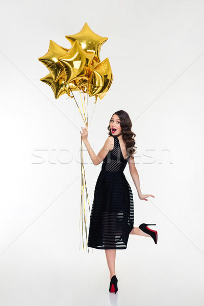 Attractive playful happy woman looking back and holding golden balloons Stock photo © deandrobot