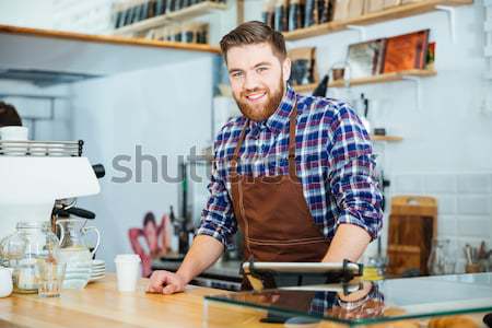 Happy handsome barista in checkered shirt and brown apron  Stock photo © deandrobot