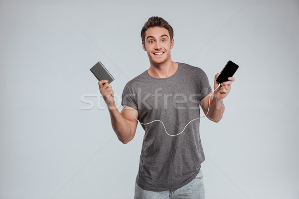 Smiling casual man charging his mobile phone Stock photo © deandrobot