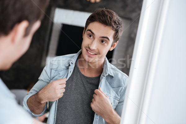 Smiling young man looking at himself in a mirror Stock photo © deandrobot
