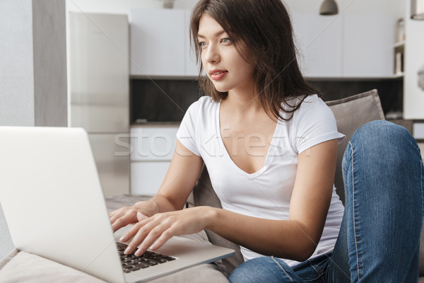 Woman sitting on sofa and using laptop at home Stock photo © deandrobot