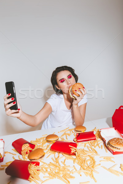 Attractive woman eating burger and taking selfie with cell phone Stock photo © deandrobot