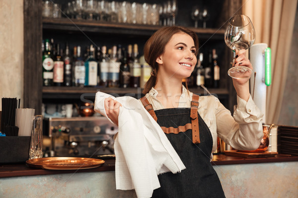 Cheerful young woman standing in cafe wipe a glass. Stock photo © deandrobot