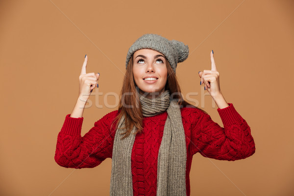 Smiling woman in winter clothes pointing with finger and looking Stock photo © deandrobot