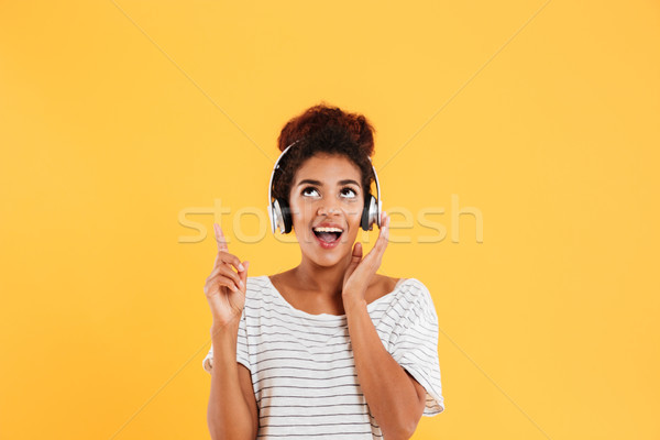 Happy african lady in headphones looking and pointing up at copy space isolated Stock photo © deandrobot