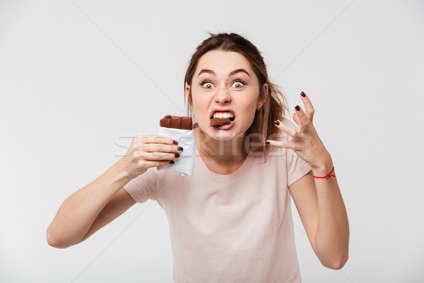Portrait of a hungry crazy girl biting chocolate bar Stock photo © deandrobot