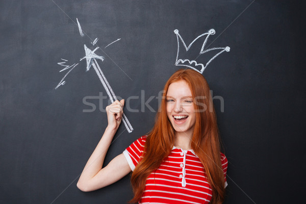 Cute woman winking with crown and magic wand over chalkboard  Stock photo © deandrobot