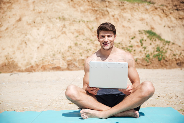 Cheerful young man using laptop on the beach Stock photo © deandrobot