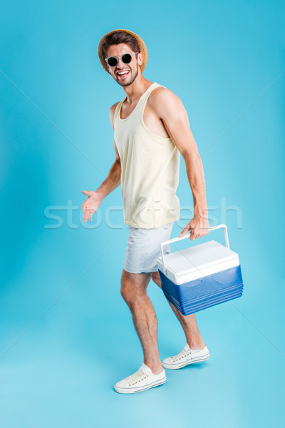 Smiling young man walking and holding cooler bag Stock photo © deandrobot