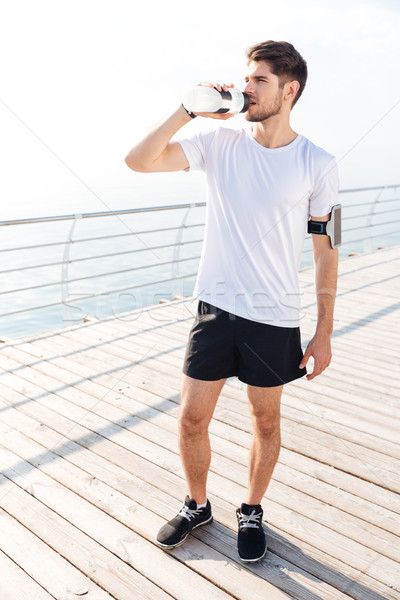 Young sportsman standing and drinking water outdoors Stock photo © deandrobot