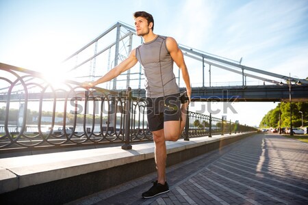 Handsome sports man running along modern bridge at sunset light Stock photo © deandrobot