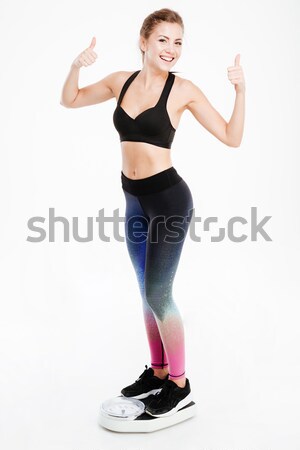Sportswoman standing on weigh scale and showing thumbs up sign Stock photo © deandrobot