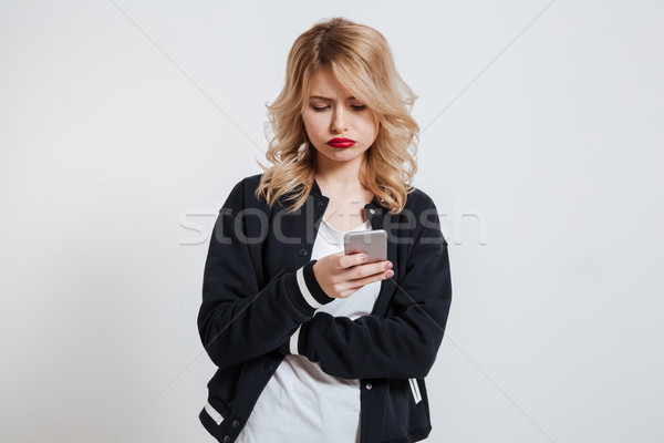 Unhappy frowning young woman using smartphone Stock photo © deandrobot
