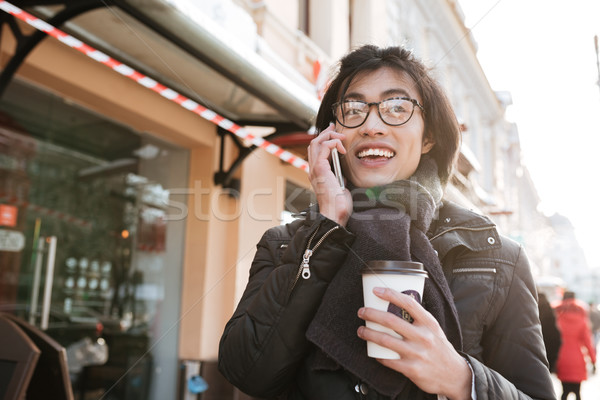 Amazing young asian man drinking coffee and talking by phone. Stock photo © deandrobot