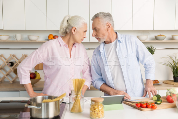 Angry mature man standing near mature serious woman at kitchen Stock photo © deandrobot