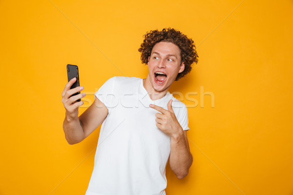 Photo of cheerful man with curly hair smiling and pointing finge Stock photo © deandrobot