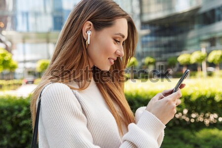 Beautiful woman sitting on the outdoor bench and typing on the phone Stock photo © deandrobot