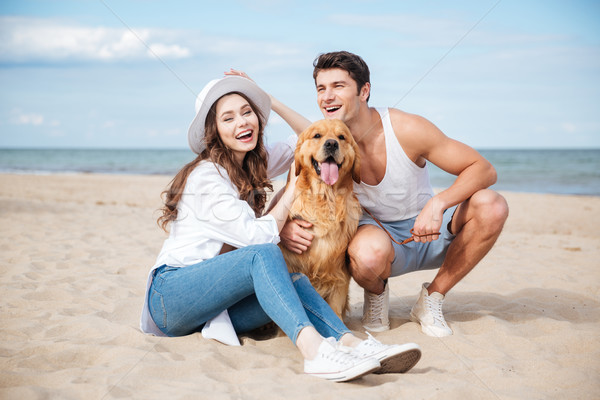 Young attractive couple with a dog sitting on the beach Stock photo © deandrobot