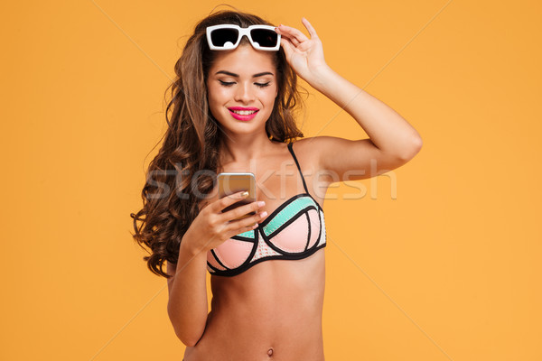Stock photo: Young sexy girl in bikini using smartphone and holding suglasses