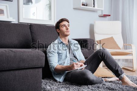 Man making notes in copybook while sitting on the carpet Stock photo © deandrobot