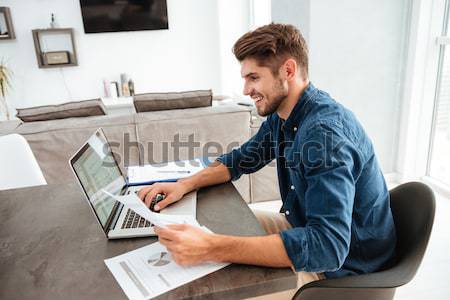 Férfi laptopot használ néz papírok fotó gépel Stock fotó © deandrobot