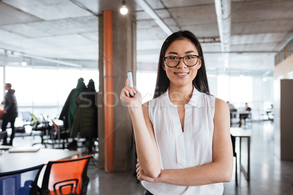 Smiling young businesswoman standing and holding whiteboard merker in office Stock photo © deandrobot