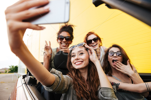 Smiling emotional four young women friends sitting in car Stock photo © deandrobot