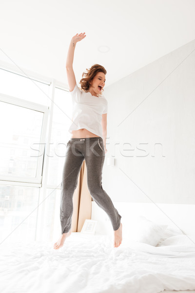 Happy amazing young woman in bed indoors jumping Stock photo © deandrobot