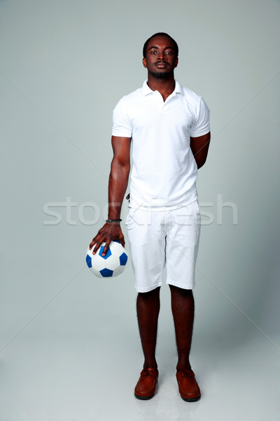 Full length portrait of a serious african man standing with soccer ball on gray background Stock photo © deandrobot