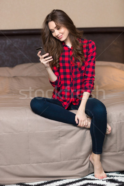 Woman sitting on the bed and using smartphone at home Stock photo © deandrobot